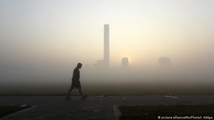 A lone man walking at dawn, smog covers the cityscape in the background